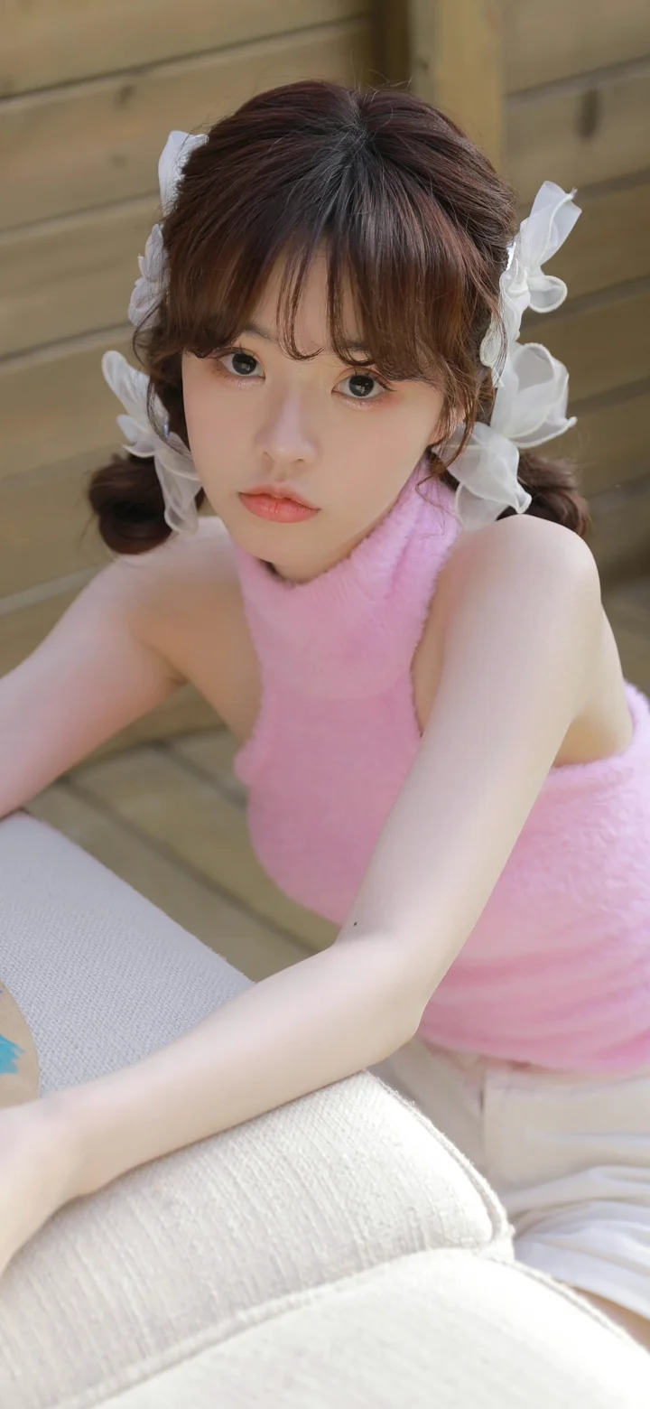 분홍색 민소매 상의를 입은 여성이 실내에서 카메라를 바라보고 있습니다.
