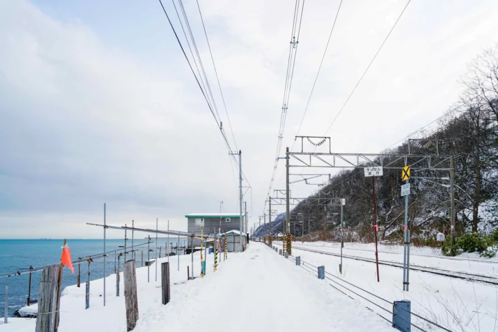 白雪覆盖的海岸旁延伸着铁路轨道， overhead电线架设在冬日天空下。