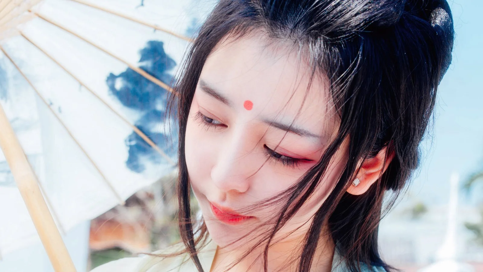 검은 머리의 여성이 옅은 색 양산 아래에서 눈을 감고 고개를 숙이고 있으며 이마에 붉은 장식이 있다.