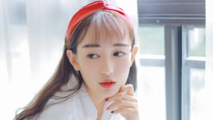 빨간 머리띠와 흰색 상의를 착용한 여성이 밝은 창가에서 옆을 바라보고 있습니다.