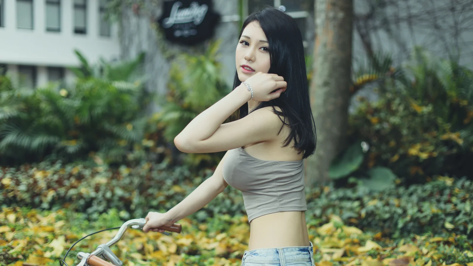 一名长发女子在绿意盎然的户外花园中靠近自行车摆姿势。