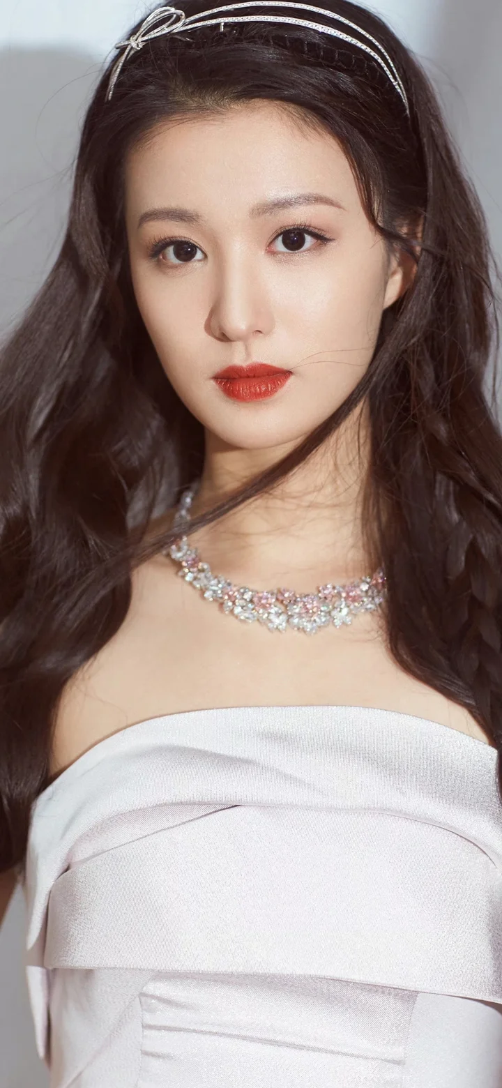 목걸이를 착용한 긴 머리 여성이 흰색 오프숄더 드레스를 입고 카메라를 바라보고 있습니다.