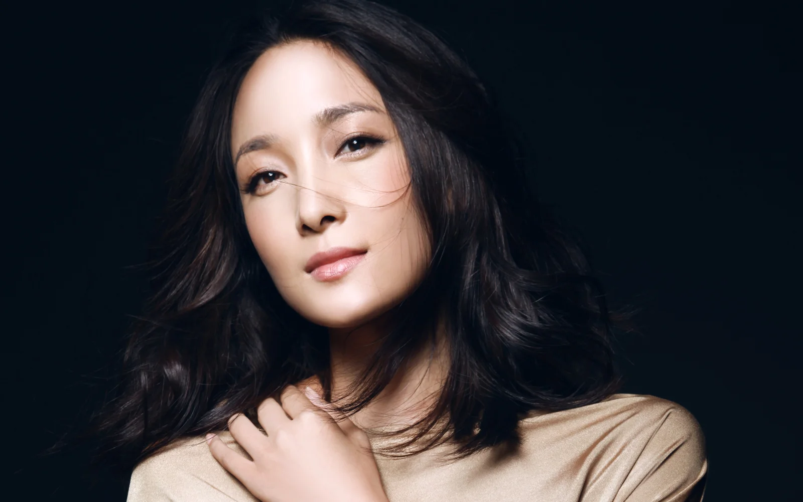 어두운 배경 앞에서 성인 여성이 카메라를 바라보는 부드러운 스튜디오 인물 사진입니다.