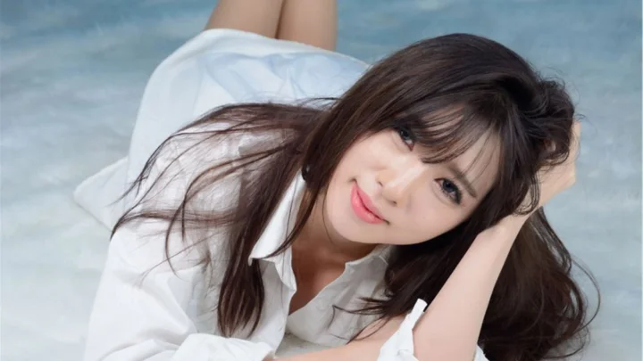 一位长发成年女性穿着白色衬衫侧躺在浅色表面上。