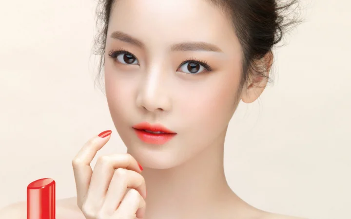 一名女性的近距离肖像，面部妆容精致，涂着红色口红，旁边可见一支口红。