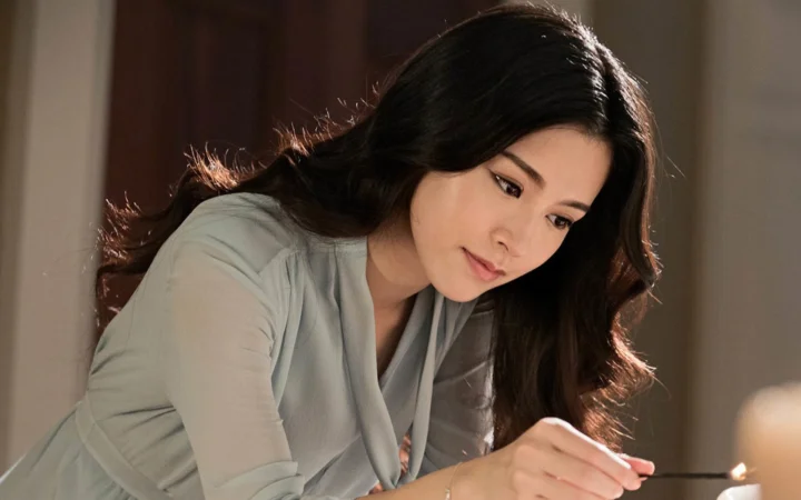 긴 머리의 여성이 실내에서 화면 오른쪽 아래의 작은 광원 쪽으로 몸을 기울이고 있다.