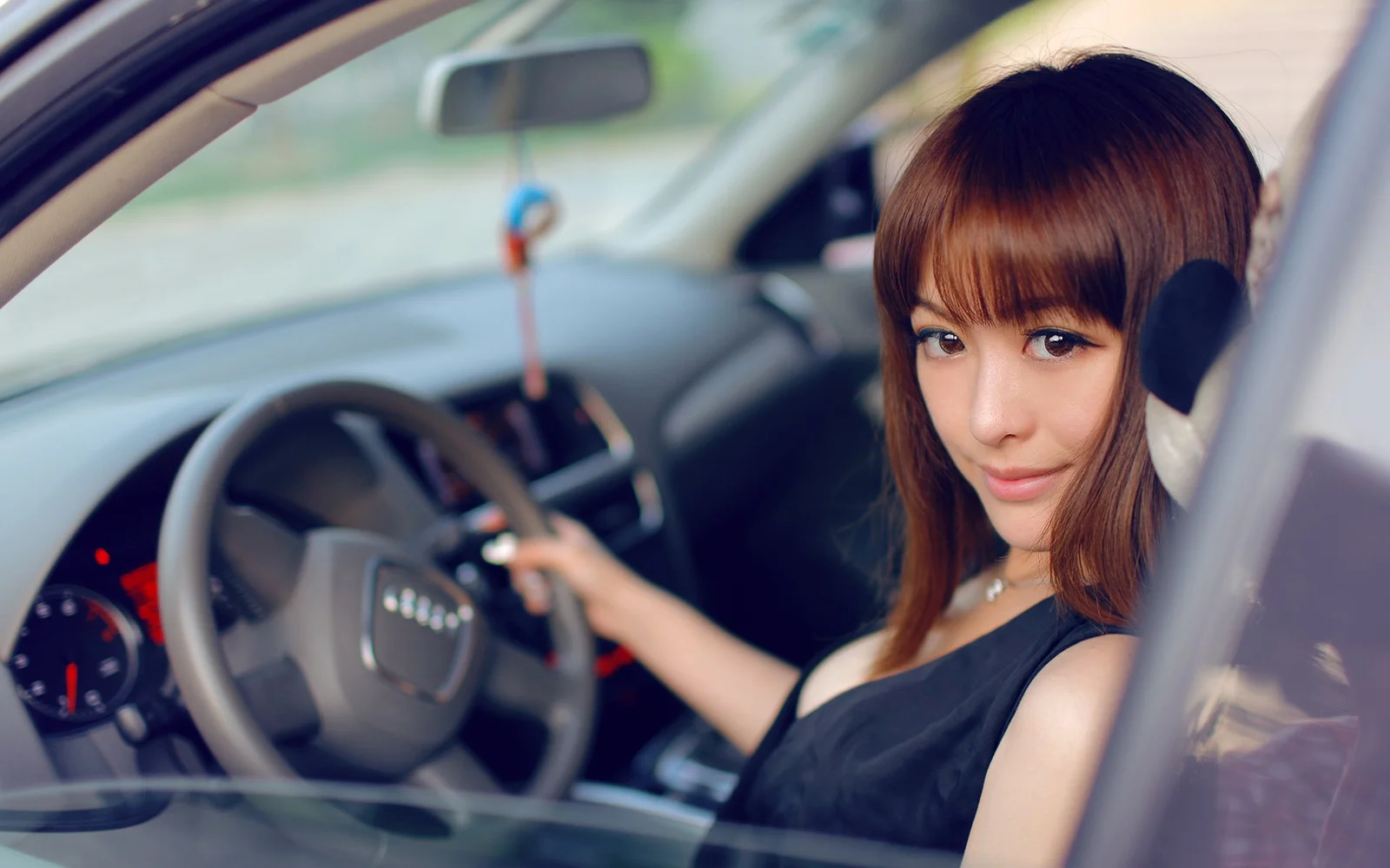 一名棕色长发女性坐在汽车驾驶座内，透过车窗看向镜头。