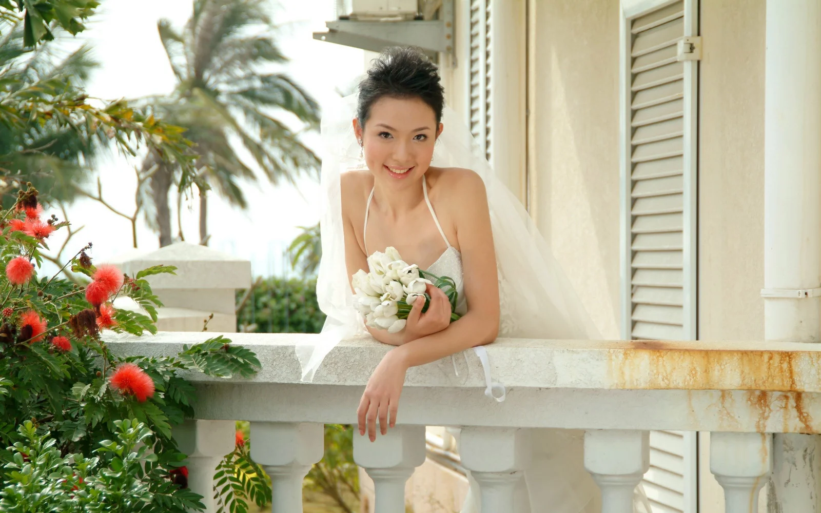 一位身穿白色婚纱、手捧花束的成年女性站在热带阳台上。