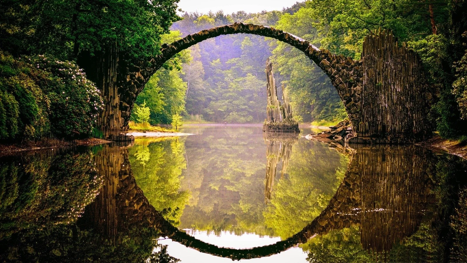 一座古朴的石拱桥横跨宁静的森林水面，倒影清晰可见。