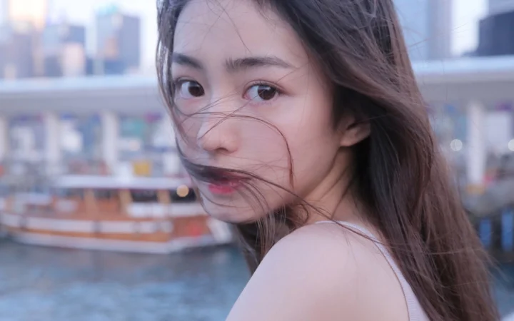 一位女性在模糊的城市背景前回望镜头，长发被风吹拂。