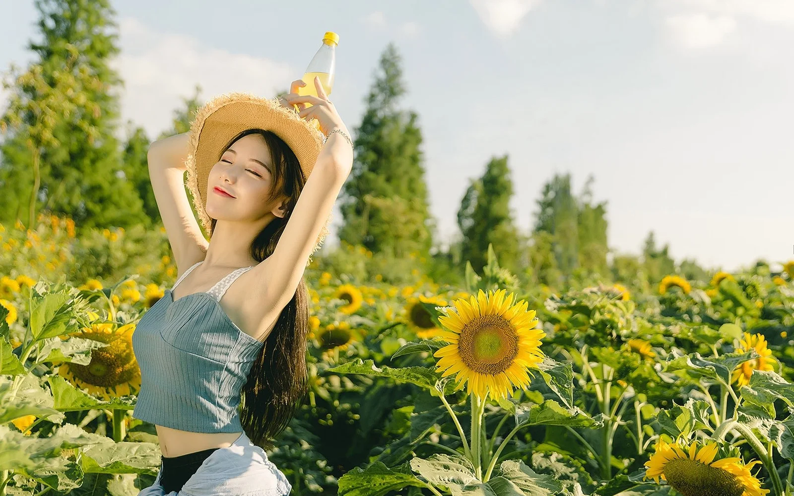 一名戴草帽的女子站在阳光明媚的向日葵花田中。