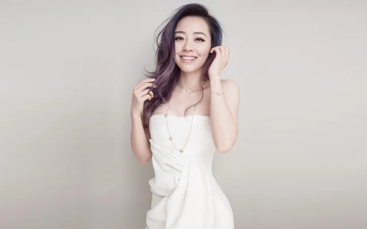 一位身穿白色抹胸连衣裙的成年女性在浅灰色背景前微笑摆姿势。