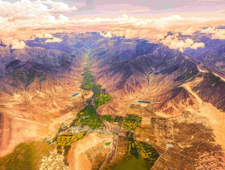 俯瞰壮阔的山脉、荒漠山谷、农田与云层交织的自然景观。