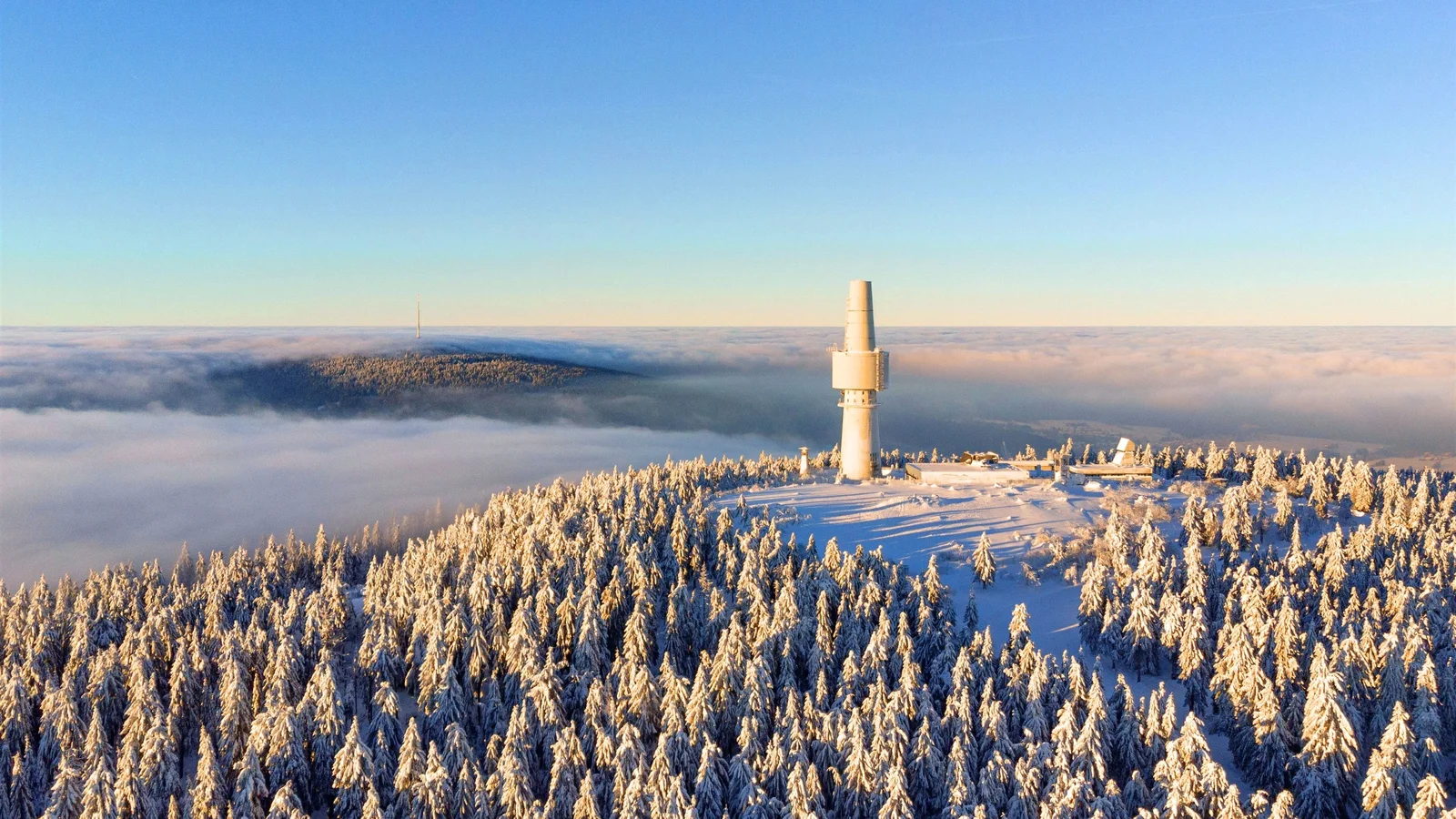 积雪覆盖的森林延伸至山脊，一座高塔矗立在云海之上。