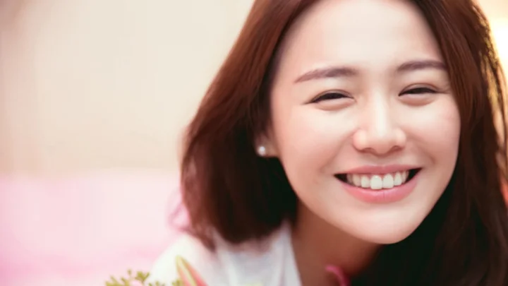 一位成年女性近距离面对镜头微笑，背景柔和虚化。