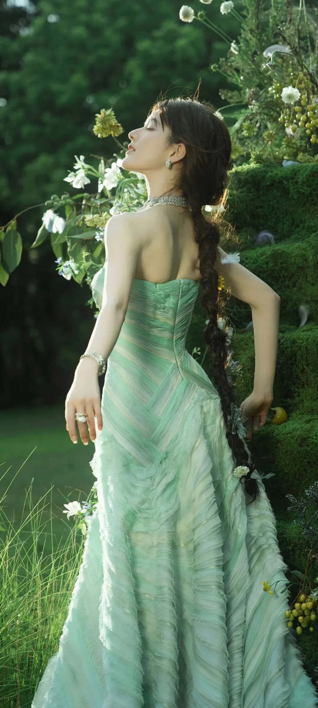 緑色のドレスを着た女性が、花や緑に囲まれた庭に立っています。