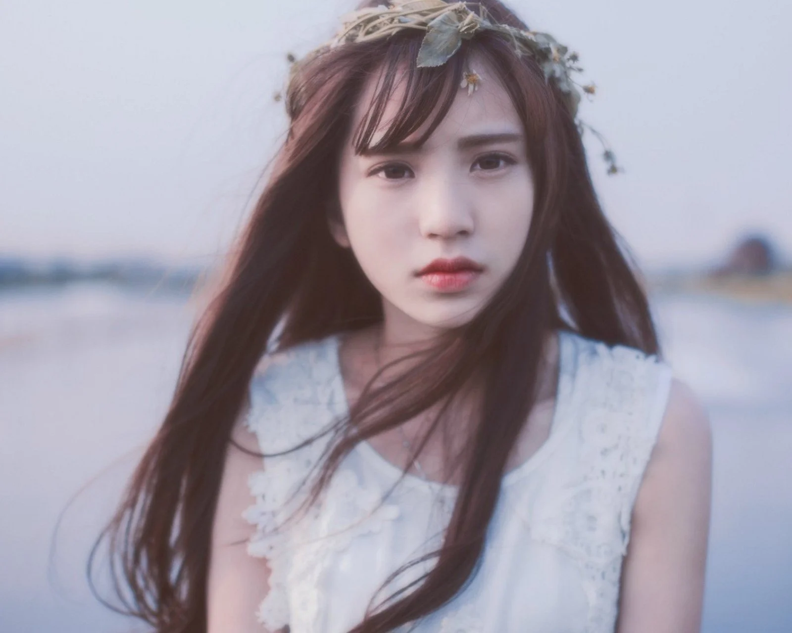 一名戴着花冠、留着长发的女子站在水边。