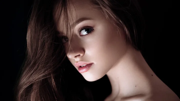 一名成年女性在黑色背景前侧脸凝视镜头。