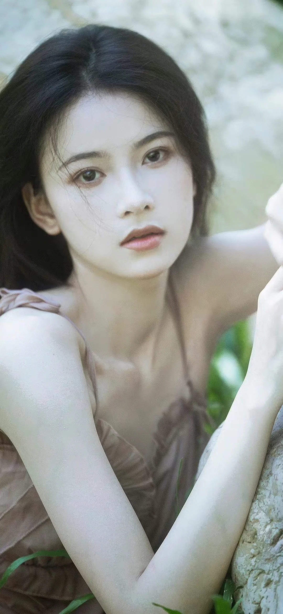 긴 머리의 여성이 나무 곁에서 자연스럽게 카메라를 바라보고 있습니다.