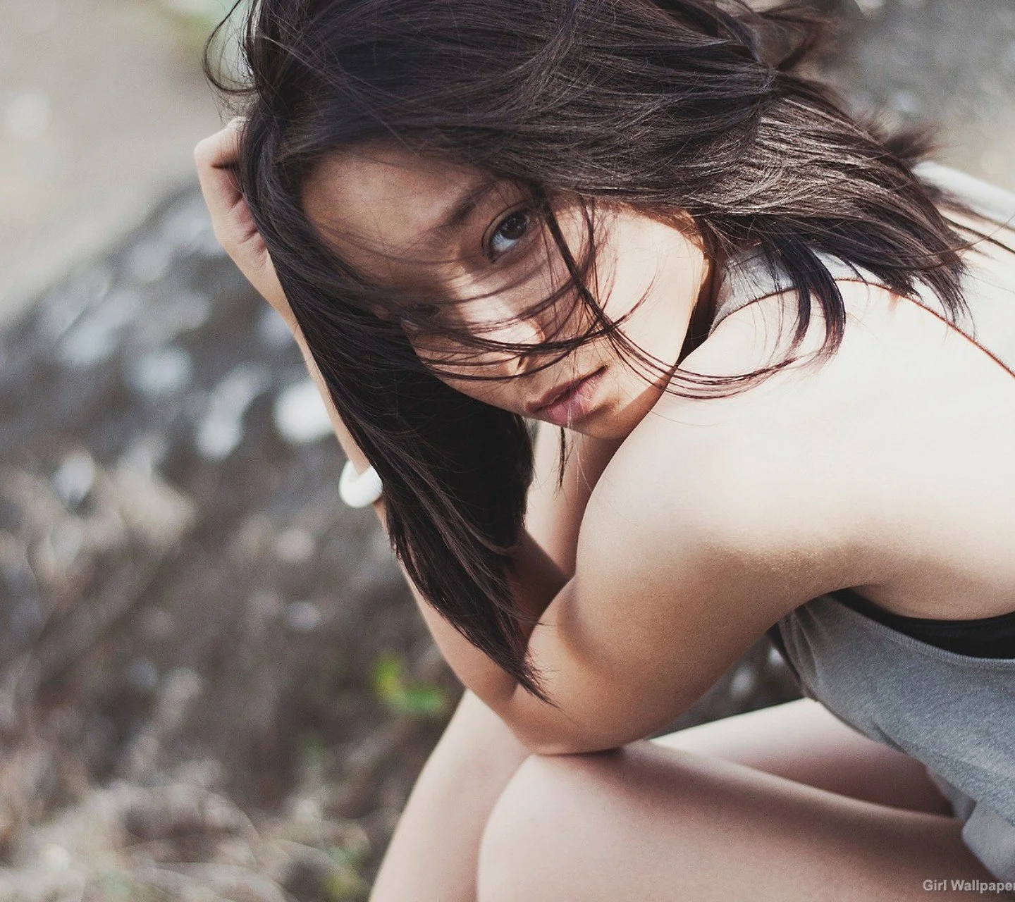 바람에 긴 머리를 흩날리며 야외에서 고개를 숙이고 있는 검은 머리 여성.