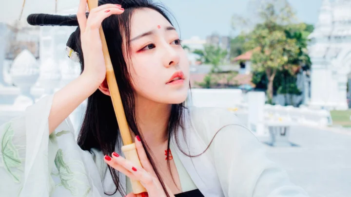 검은 머리의 여성이 야외에서 나무 손잡이 우산을 들고 옆을 바라보고 있다.