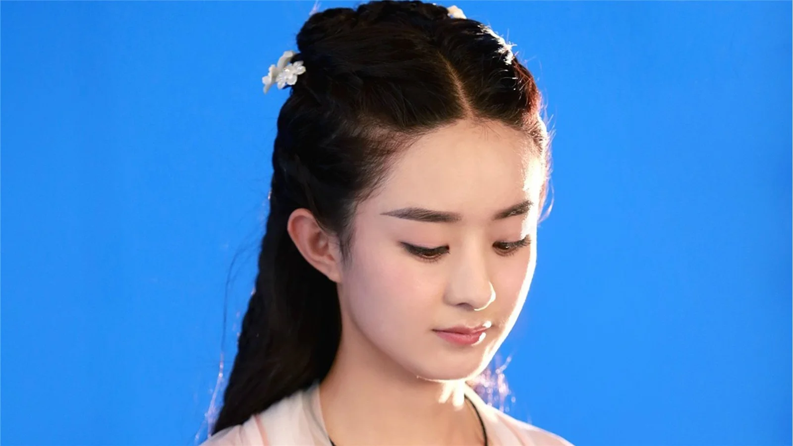一名女子在明亮的蓝色背景前低头侧望。