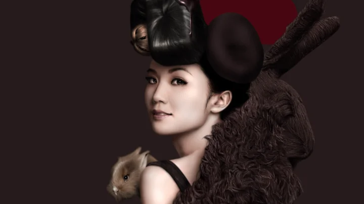 画面呈现一位留着华丽深色发饰的女性肖像，肩后带有深色毛绒质感，背景为深色。