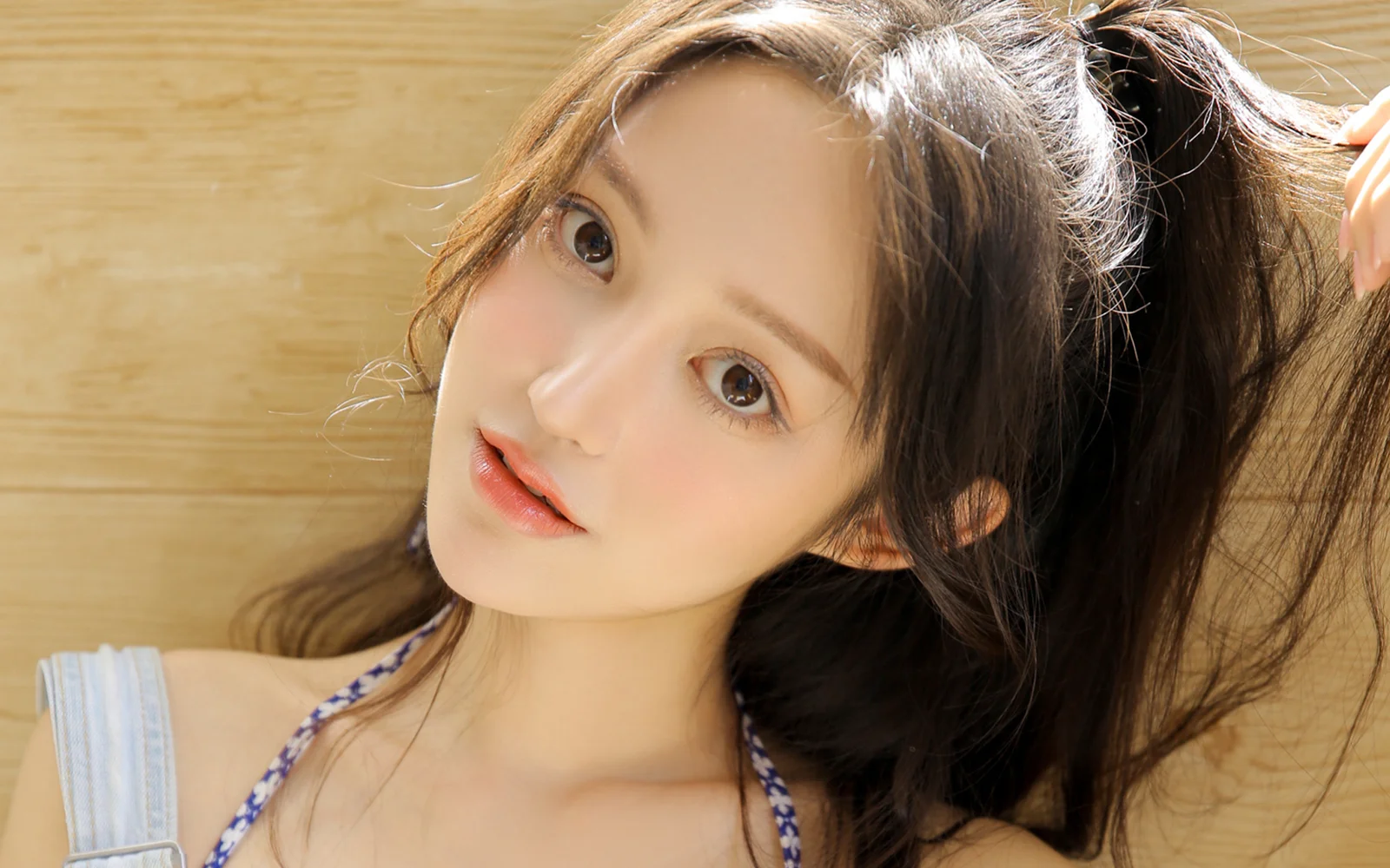 一名成年女性靠在木质背景前，抬头看向镜头并用手整理长发。