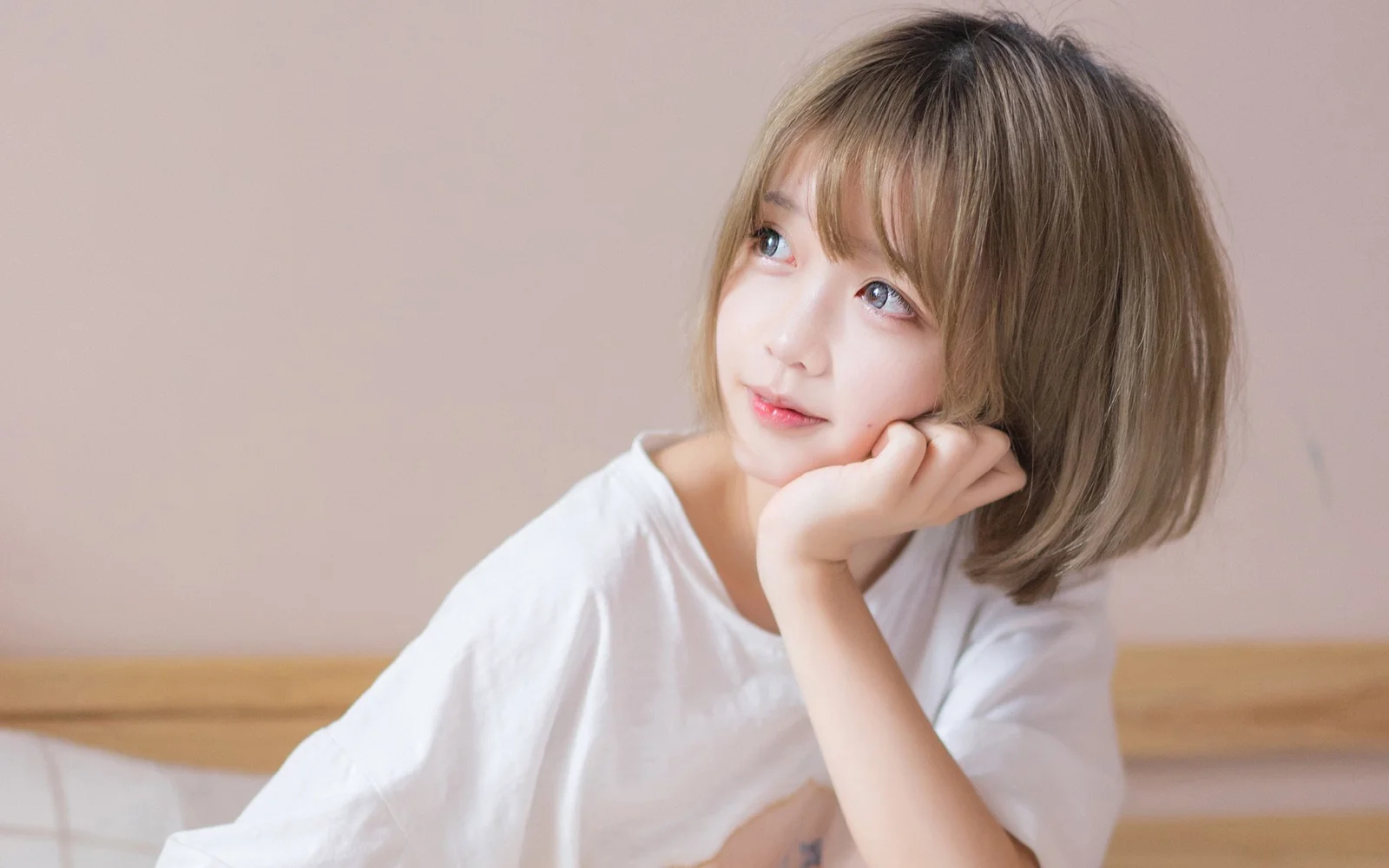 一名棕色短发女子身穿白色上衣，托腮望向镜头外。