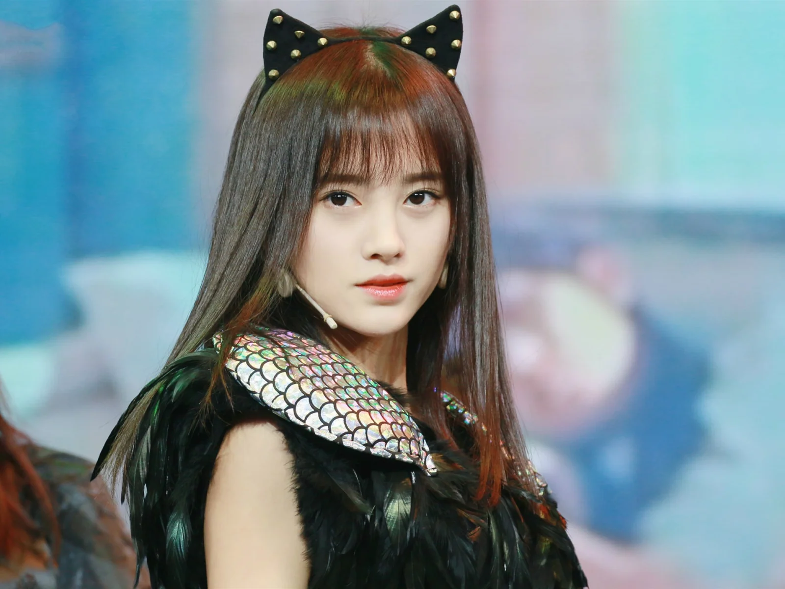 猫耳の髪飾りと黒い羽根飾りの衣装を身に着けた女性がカメラを見つめている。