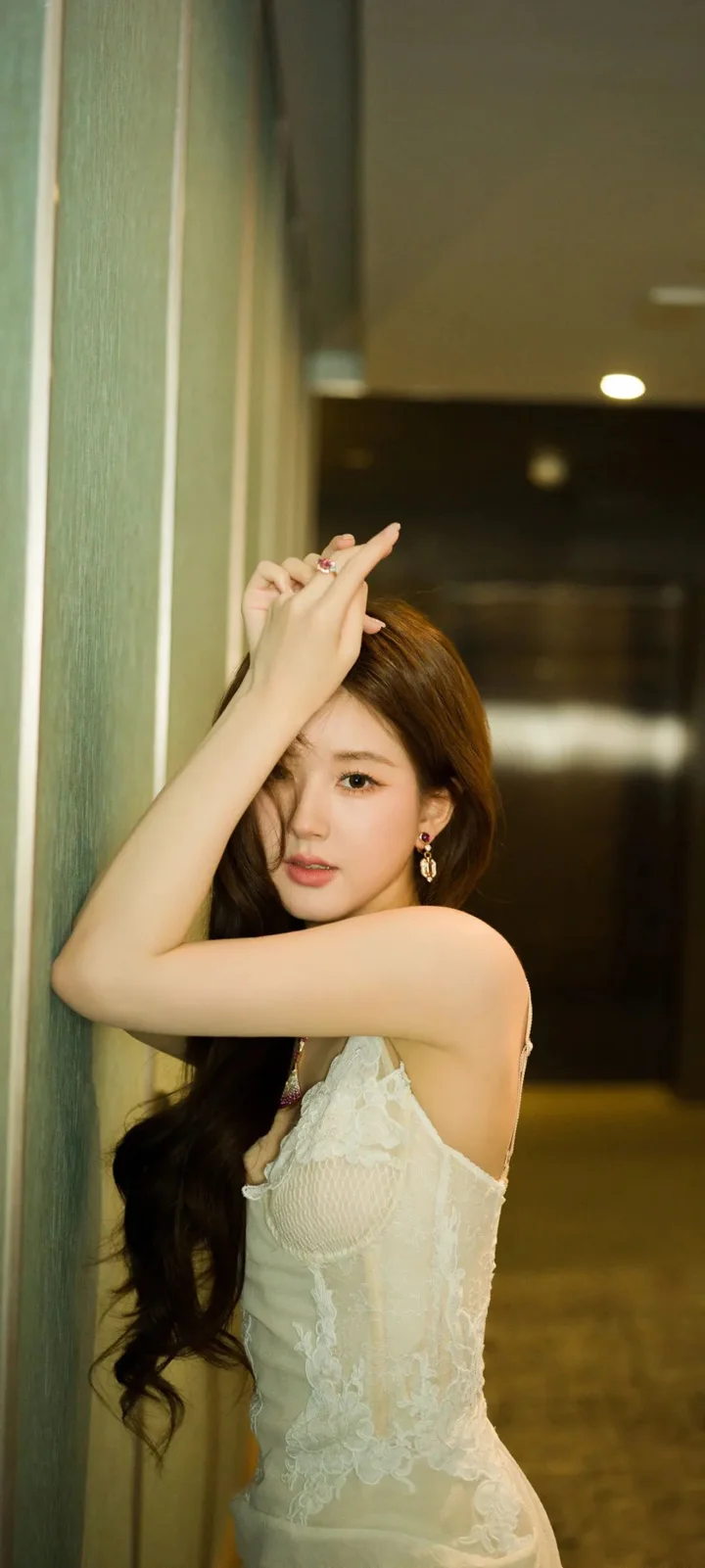 一名成年女性穿著白色蕾絲裙在室內牆邊擺姿勢。