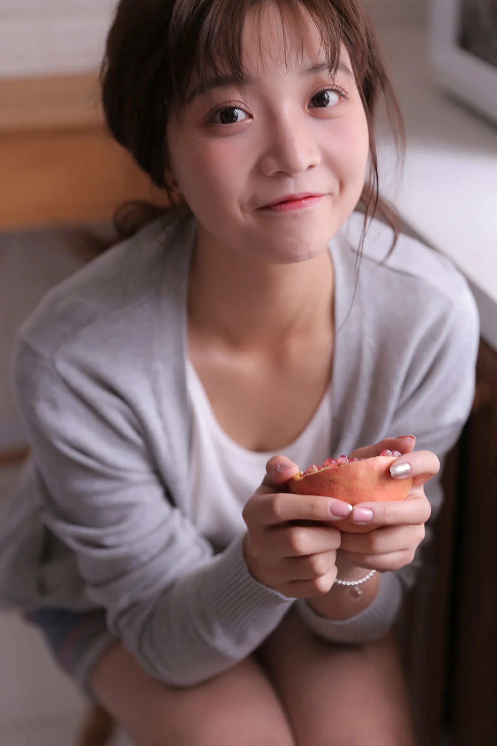 若い女性が室内でカメラに近づいて向き合い、両手で小さなカラフルな物を持っています。