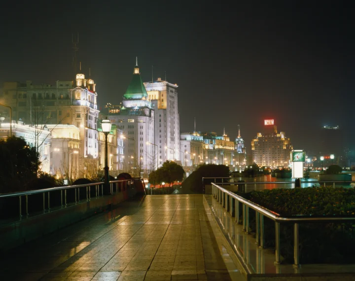 夜晚灯火映照着滨水步道、城市建筑与平静水面。