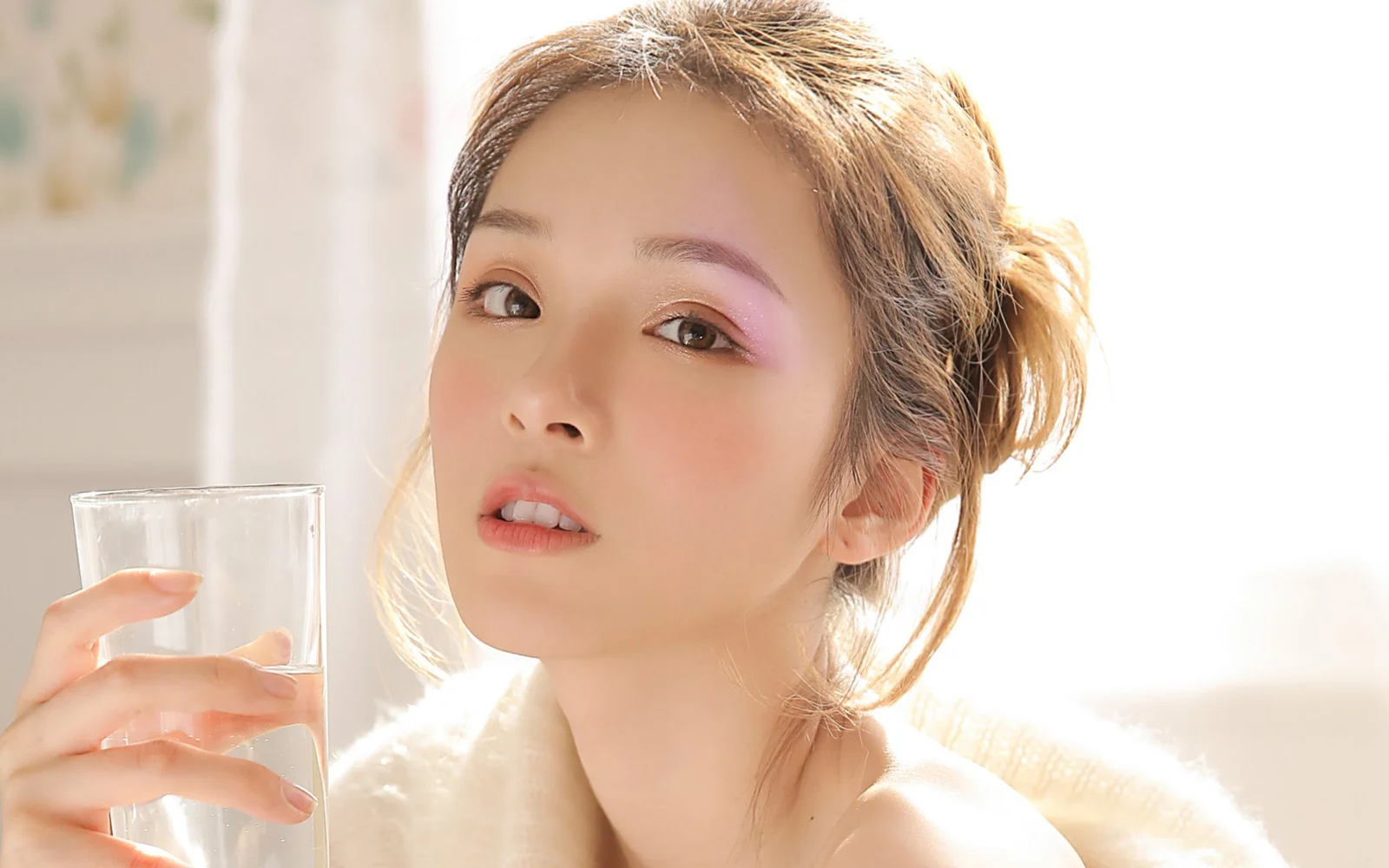 一名女性在明亮柔和的光线下手持一杯水。