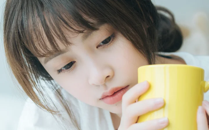 한 여성이 손에 든 밝은 노란색 컵을 내려다보고 있다.