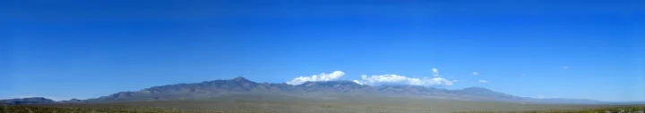 宽阔的山脉横贯地平线，远处可见积雪山峰，前景是一片低矮植被。