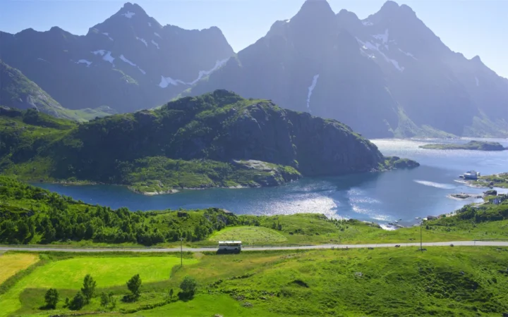 群山环抱的湖泊映照着阳光，前景是连绵的绿色山坡与道路。