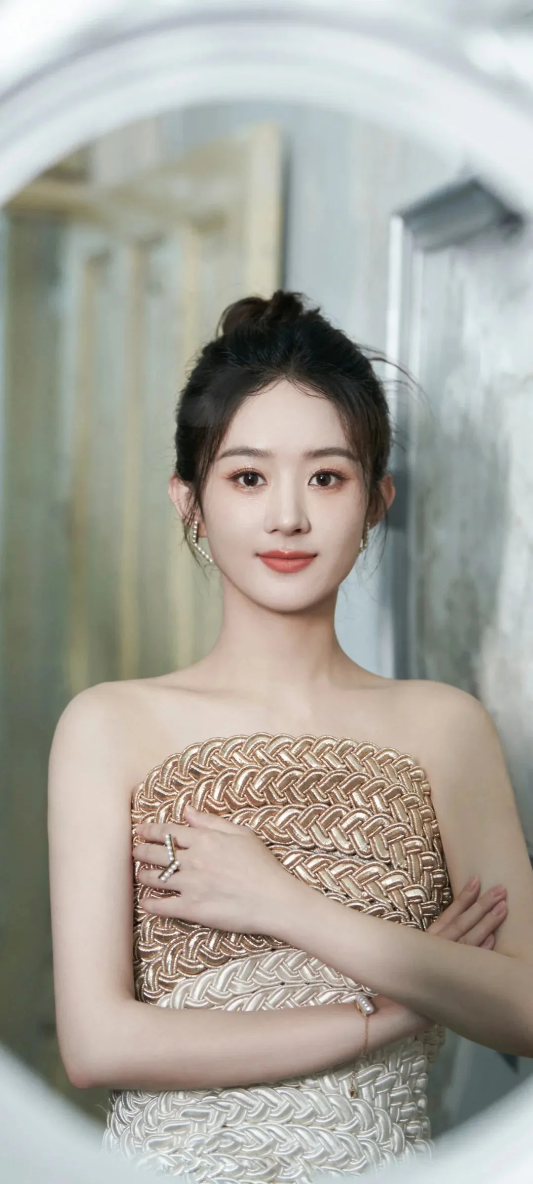 一名成年女性身穿金色编织礼服站在室内拱形镜面前。