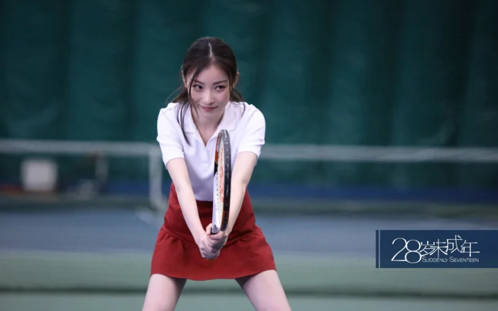 一名身穿白色上衣和红色裙子的成年女性在网球场上握着球拍。