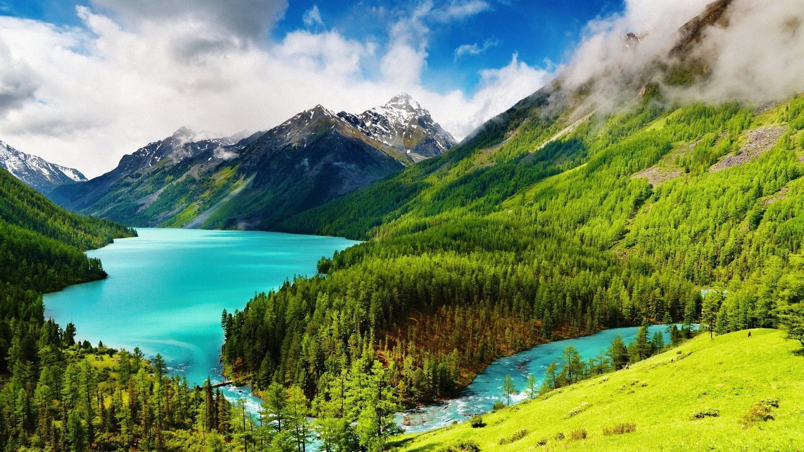 碧 turquoise 湖泊与河流环绕着茂密森林和云雾缭绕的雪山。