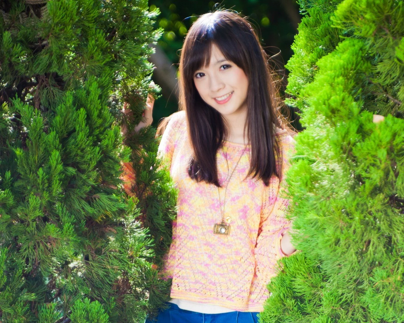 一名长发女子站在茂密的常绿树木之间微笑面对镜头。