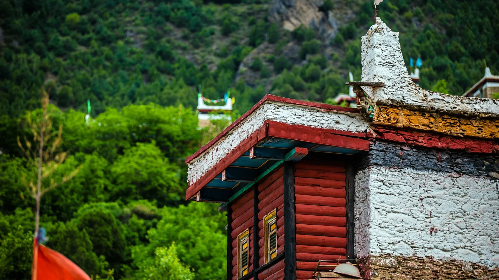 선명한 붉은색과 흰색 벽을 지닌 티베트식 건물이 울창한 산림을 배경으로 서 있다.