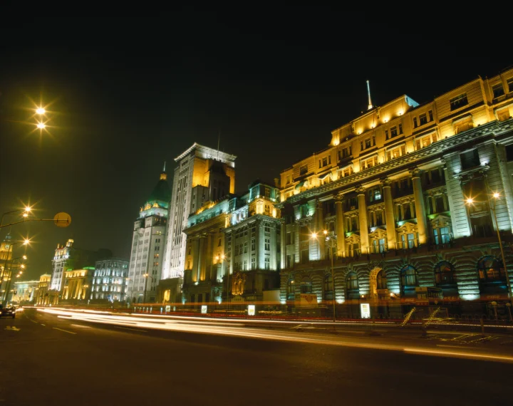 夜晚灯光照亮的城市建筑沿街排列，车流形成明亮的光轨。