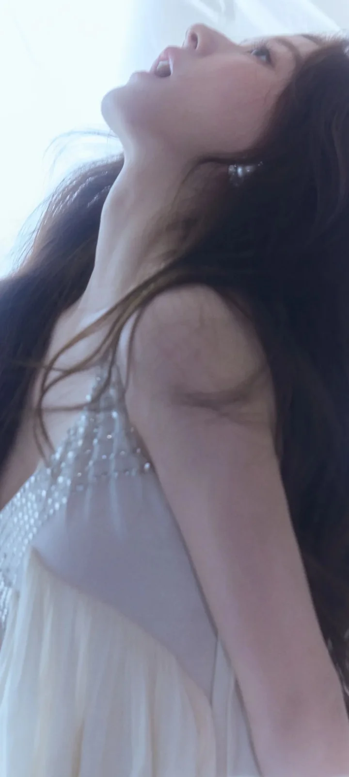 一位长发女性穿着白色连衣裙侧头仰望，沐浴在柔和的浅蓝色光线中。