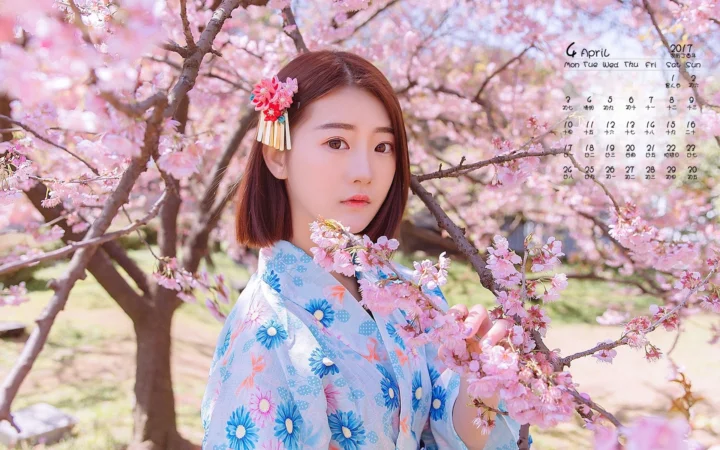 一名身穿蓝色花卉服装的女子站在盛开的樱花树间。