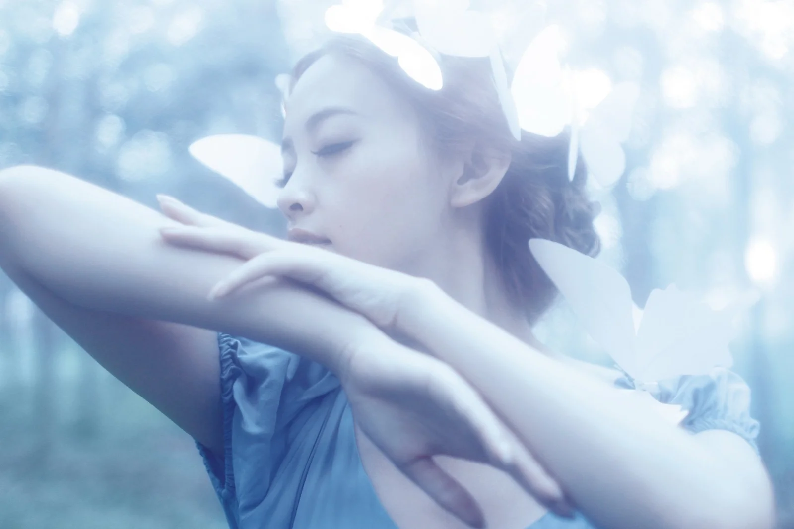 一位女性在柔和蓝色光影与白色花瓣映衬下闭眼侧身呈现梦幻肖像。