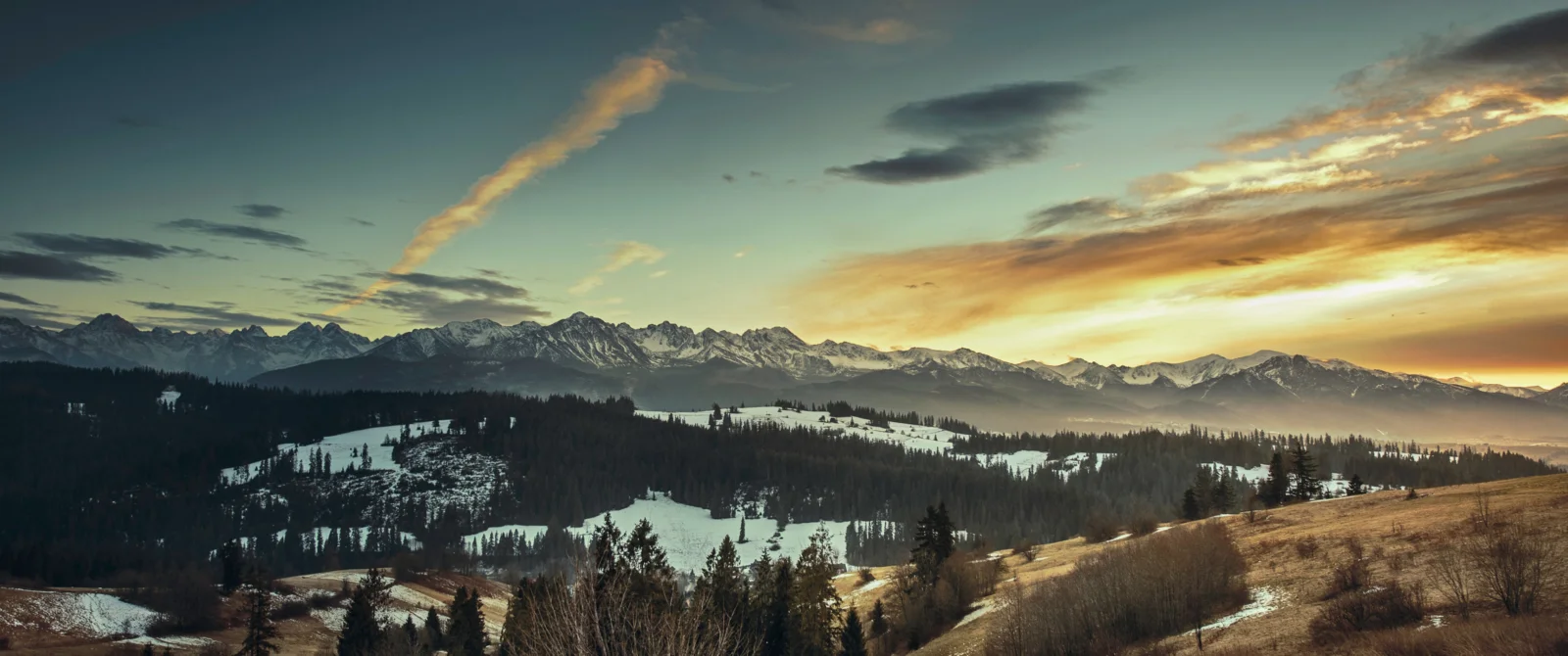 夕陽映照下的雪山、森林與起伏山坡構成壯麗的冬日全景。