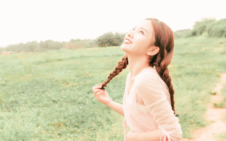 一名留着两条辫子的女子站在开阔的绿色草地中仰望天空。