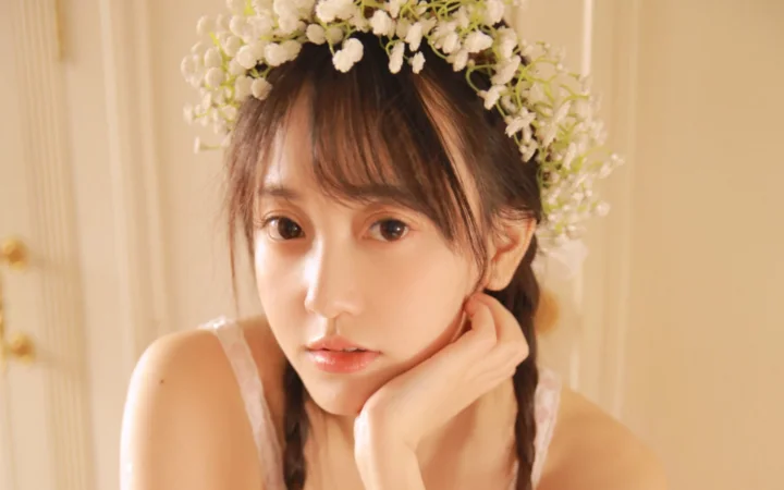 一位戴着白色花环、留着编发的女性在暖色室内光线下看向镜头。