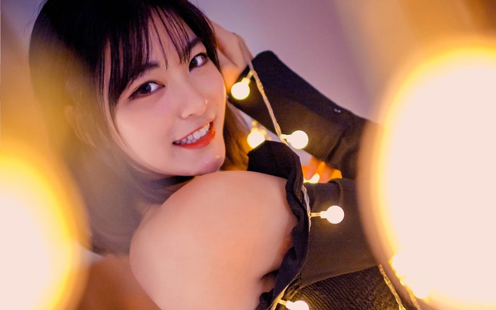 暖かな電飾と柔らかな光の中で、女性がカメラを振り返っている。